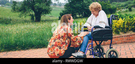 Junge Frau im Gespräch mit älteren Frau im Rollstuhl Stockfoto