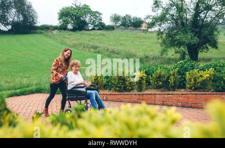 Frau, die ihre Mutter, die im Rollstuhl Stockfoto