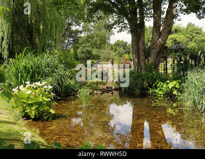 Üppigen Garten mit Bach und kleine steinerne Fußgängerbrücke Stockfoto