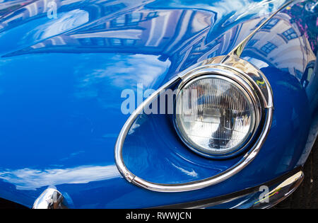 Nahaufnahme der Scheinwerfer der Jaguar E-Type-Serie 2 mit Spiegelungen alter Gebäude auf der Oldtimer-Ausstellung in Sopron, Ungarn Stockfoto