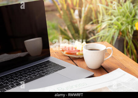 Kaffeebecher und Nachrichten Papier mit frischem Obst und Laptop auf dem Holztisch. Stockfoto