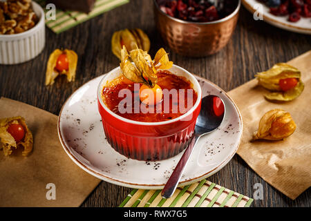 Köstliche Crème Brûlée in Rot ramekin serviert und mit Kap stachelbeeren eingerichtet Stockfoto