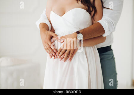 Mann seine Frau umarmt Bauch in weißem Kleid. Stockfoto