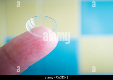 Weiche Kontaktlinsen auf Fingerspitze, Makro mit blauen und gelben Hintergrund und Tageslicht. Stockfoto