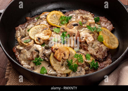 Eine Nahaufnahme von scallopine di Vitello, Kalbfleisch scallopini, ein traditionelles italienisches Gericht mit einem Pilzsauce, Zitronen, und Petersilie, in einem Schmortopf Stockfoto