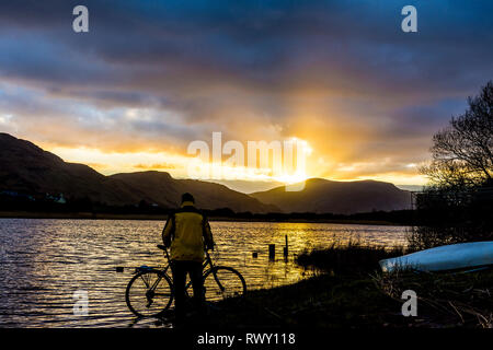 Ardara, County Donegal, Irland. 7. März 2019. Ein Radfahrer hält den Sonnenuntergang über dem See Shanaghan zu beobachten. Credit: Richard Wayman/Alamy leben Nachrichten Stockfoto