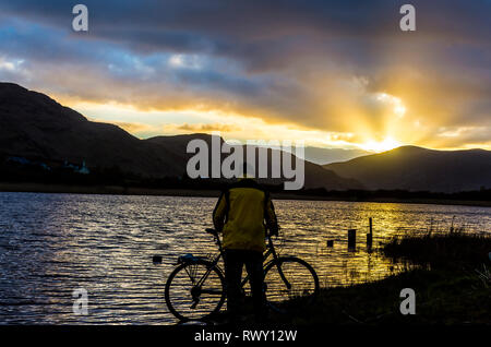 Ardara, County Donegal, Irland. 7. März 2019. Ein Radfahrer hält den Sonnenuntergang über dem See Shanaghan zu beobachten. Credit: Richard Wayman/Alamy leben Nachrichten Stockfoto