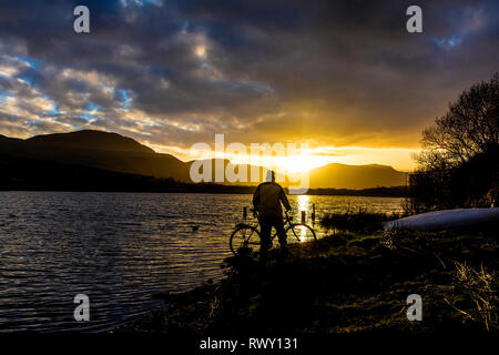 Ardara, County Donegal, Irland. 7. März 2019. Ein Radfahrer hält den Sonnenuntergang über dem See Shanaghan zu beobachten. Credit: Richard Wayman/Alamy leben Nachrichten Stockfoto