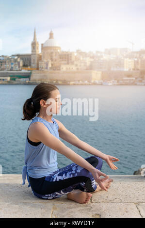 Seitenansicht einer Frau, meditieren, Yoga mit Valletta, Malta als Hintergrund Stockfoto