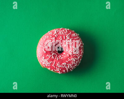 Blick von oben auf die rosa glasierten Krapfen auf grünem Hintergrund. Verglast und Topping beträufeln rosa Donut auf das reiche grün hinterlegt. Top View oder flach. Stockfoto