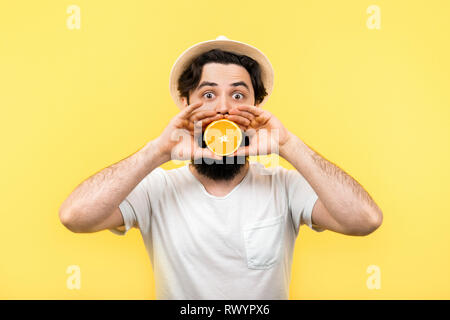 Studio Portrait einer überrascht, bärtigen Mann hält die Hälfte der orange Zitrusfrüchten in die Hände, die seinen Mund auf gelben Hintergrund, Sommerlaune, happin Stockfoto