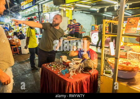 Europäische Mann bittet um Wegbeschreibungen von asiatischen Straße Verkäufer in der Jalan Alor, Kuala Lumpur, Malaysia Stockfoto