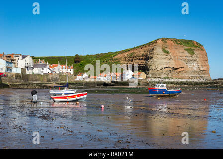 Staithes Hafen an der Küste von North Yorkshire, England. Einen sonnigen Frühling Morgen in dieser malerischen Fischerdorf. Mann Graben für wattwürmer. Stockfoto