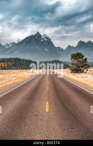 Highway vor der schroffen Berge mit bewölktem Himmel, Grand Teton Bergkette, Grand Teton National Park, Wyoming, USA Stockfoto