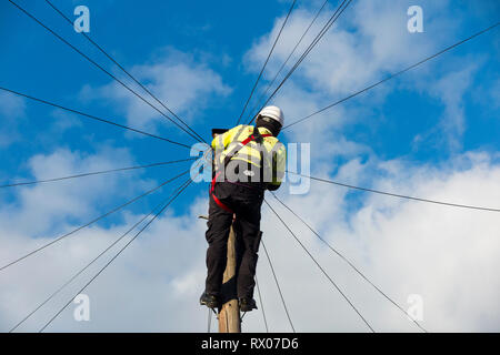 Telecom Engineer, der an inländische Telefonleitung/Breitband Internet Kupferdraht ein Telefon/Telegraphenmast in einem Londoner Straße, & blauer Himmel Stockfoto