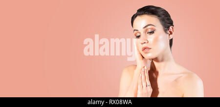 Young woman with clear skin touching with hands her face against pastel coral color background. Stockfoto