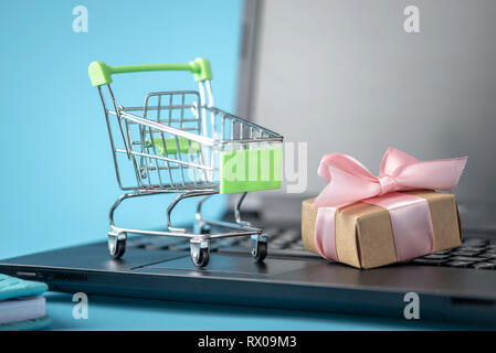 Warenkorb und Geschenkbox Preis auf dem Laptop Tastatur auf einem blauen Hintergrund. Das Konzept der Rabatte und Shopping in Online Shops Stockfoto