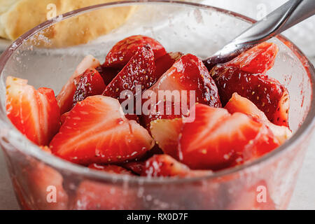 Nahaufnahme von in Scheiben geschnittene Erdbeeren in klaren Glasschale glasiert mit Zucker. Löffel in der Schüssel. Stockfoto