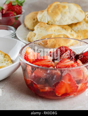 Schale in Scheiben geschnittene Erdbeeren glasiert mit Zucker. Gebäck, Zucker, und ganze Erdbeeren unscharf im Hintergrund. Stockfoto