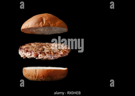 Flying Burger mit Brötchen und Fleisch isoliert auf Schwarz Stockfoto