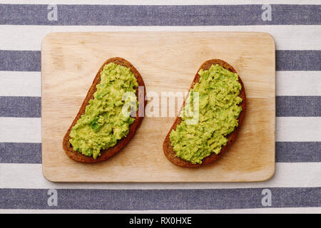 Guacamole Sandwich auf hellen Hintergrund avocado Sandwiches auf Holzbrett und textile Draufsicht Stockfoto