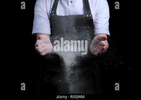 Hände und Mehl im Splash baker klatschen auf schwarzem Hintergrund Stockfoto