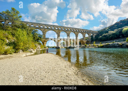 Ein paar stehen am Strand an einem Ufer des Gardon River in der Provence, Frankreich mit der antiken römischen Aquädukt Pont du Gard im Hintergrund Stockfoto