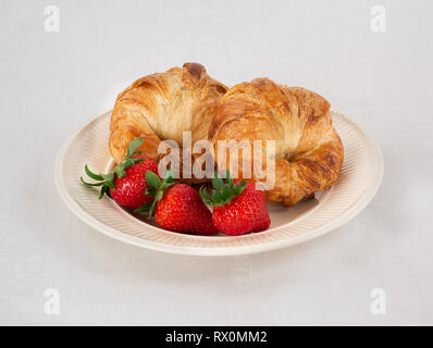 Cremefarbene Platte mit zwei Croissants und Drei frische Erdbeeren auf einem weißen Leinen Tischdecke. Stockfoto