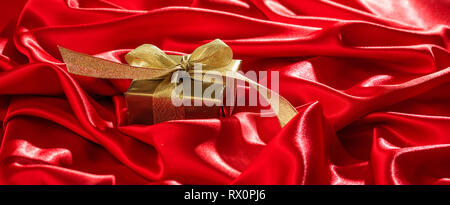 Weihnachtsgeschenke. Goldenen Geschenkkarton mit Gold Ribbon Rot Satin Hintergrund, Banner, kopieren Raum Stockfoto