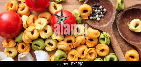 Italienisches Essen Vorbereitung. Bunte tortellini Pasta, Tomaten und Knoblauch auf Holztisch, Banner, Ansicht von oben Stockfoto