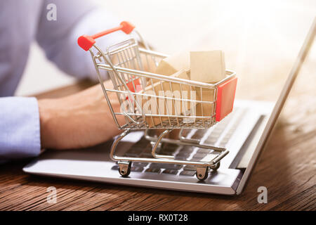 Nahaufnahme der Mann mit Laptop mit Miniatur Kartons In den Einkaufswagen Stockfoto