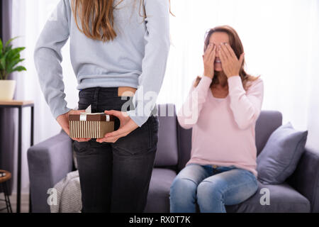 Mädchen verstecken Geschenk von Ihrer Mutter sitzt auf einem Sofa und die Augen Stockfoto