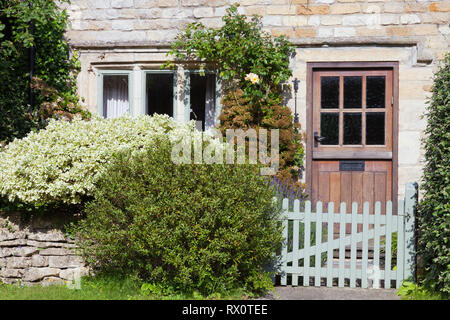 Dunkle braune Türen in einem alten traditionellen Englischen Kalk Steinhaus mit Sträuchern in einem kleinen Garten mit Trockenmauern Zaun, Holz- tor. Stockfoto