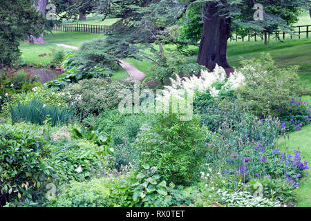 Kiesweg durch üppige Englischer Garten mit Blumen, Büschen, alten Bäumen. Stockfoto