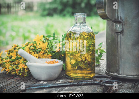 Hypericum - Johanniskraut Pflanzen, Öl oder Infusion transparente Flasche, Mörtel auf hölzernen Tisch im Freien. Stockfoto