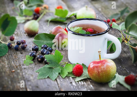 Emaillierte Schale von Obst Tee mit Äpfeln, Birnen, Himbeeren und schwarzen Johannisbeeren Beeren auf hölzernen Tisch im Freien. Stockfoto