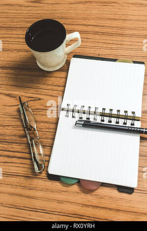 Schreibtisch mit offenen Notebook mit leeren Seiten, Brillen, Kugelschreiber und einer Tasse Kaffee. Ansicht von oben mit der Kopie. Business still life Konzept mit Office stuf Stockfoto