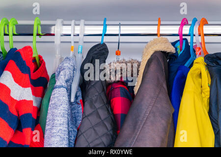 Der kleine Junge Kind größe Jacken, Mäntel und Pullover hängen in den Schrank ein Kinderparadies mit bunten Kleiderbügel. Vorbereitung für den Winter mit warme Kleidung für Kinder. Stockfoto