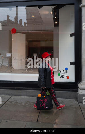 Ein shopper Spaziergänge hinter einem Fenster angezeigt, die Teil einer Design 'State der Künste" genannt, im Kaufhaus Selfridges in der Oxford Street, am 4. März 2019 in London, England. Zustand der Kunst ist eine Galerie mit Werken von neun crtically-anerkannten Künstlern in Selfridges, um die Macht der öffentlichen Kunst feiern Jeder der Künstler sind in der Erstellung einer Site-spezifischen Kunstwerk an einem der neuen Elizabeth Linie Stationen als Teil der Traverse Art Programm beteiligt. Stockfoto