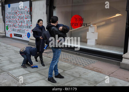 Eine asiatische Familie Kampf mit einem blauen Boot außerhalb eines Fensters angezeigt, die Teil einer Design 'State der Künste" genannt, im Kaufhaus Selfridges in der Oxford Street, am 4. März 2019 in London, England. Zustand der Kunst ist eine Galerie mit Werken von neun crtically-anerkannten Künstlern in Selfridges, um die Macht der öffentlichen Kunst feiern Jeder der Künstler sind in der Erstellung einer Site-spezifischen Kunstwerk an einem der neuen Elizabeth Linie Stationen als Teil der Traverse Art Programm beteiligt. Stockfoto