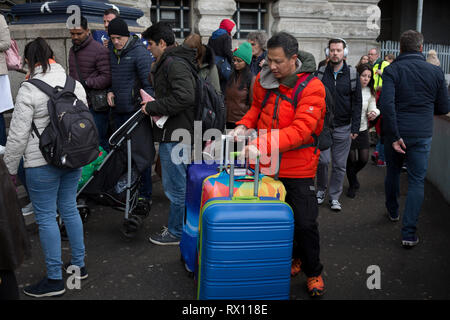 Eine touristische Räder bunte Koffer am Abend rush-hour neben normalen Pendler an der Waterloo Station verhandelt, am 4. März 2019 in London, England. Stockfoto