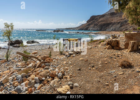 Tisch und Stühle in der Sonne am Strand mit Blick auf das Meer auf der Insel Kreta, Griechenland Stockfoto