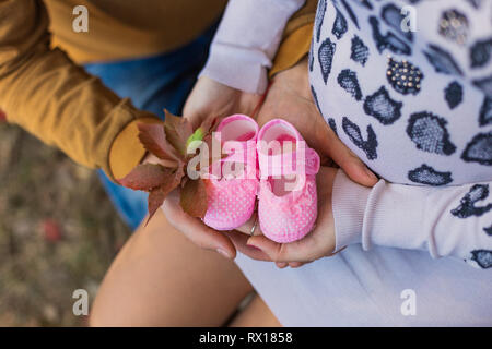 Schwangerschaft. Der Bauch einer schwangeren Mädchen und ihrem Ehemann. Der Mann hält seine Hand auf den Bauch Frau mit Schuhe für Babys. Stockfoto