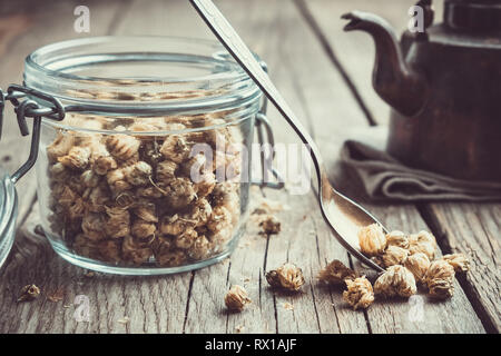 Glas Glas trockener gesunde Kamille Knospen, Löffel und vintage Teekanne auf Alte n Holztisch. Die Kräutermedizin. Stockfoto