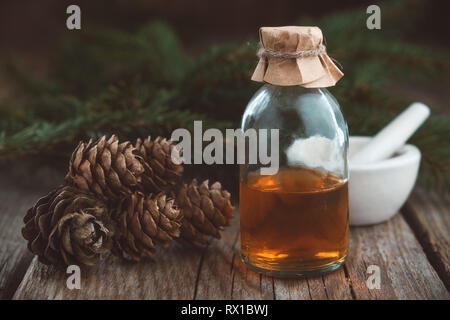 Tanne aromatische Öl. Kiefer ätherisches Öl in einer Glasflasche, Fichte Kegel, Nadelholz Zweigen und Mörtel. Stockfoto