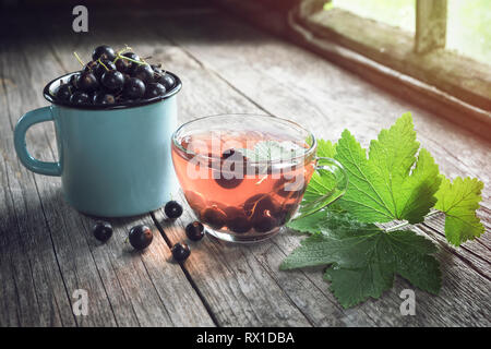 Becher von schwarzen Johannisbeeren, Glas Tasse Früchtetee mit Schwarze Johannisbeere Beeren auf Holz- Tabelle innerhalb der retro Haus im Dorf. Stockfoto