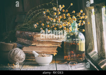 Mörtel von getrockneten Kräutern, eine Flasche Öl- oder Infusionslösung, alte Bücher und Bündel trockenen Kamille Anlage. Die Kräutermedizin. Stockfoto