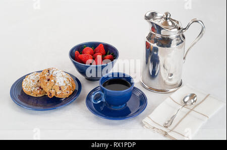 Frühstück mit Gebäck auf einem dunkelblauen Teller und Schale frische Erdbeeren mit Kaffee und einem silbernen Hotel Zimmer Service Karaffe auf weißem Leinen Tischdecke Stockfoto