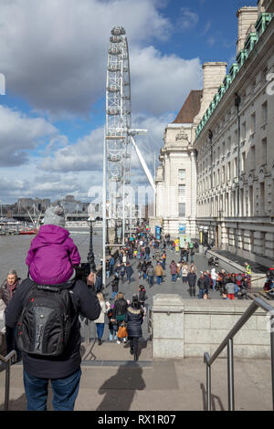 Die Eltern und das Kind zu Fuß die Schritte in Richtung South Bank, Richtung London Eye, London, UK, auf einem kalten, veränderbar und blustery Mittags im März. Stockfoto