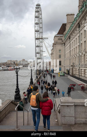 Junges Paar zu Fuß die Schritte in Richtung South Bank, Richtung London Eye, London, UK, auf einem kalten, veränderbar und blustery Mittags im März. Stockfoto